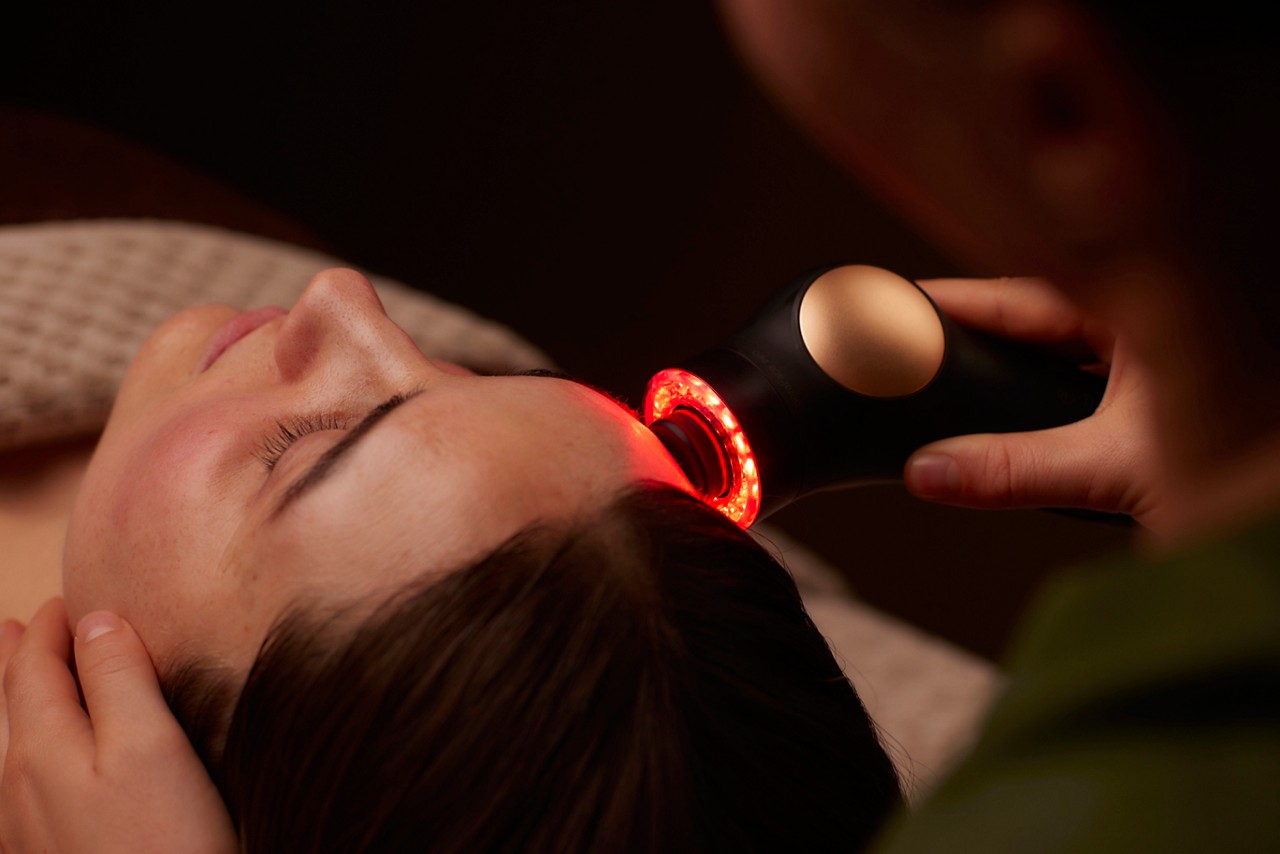 Spa therapist giving a woman a Theraface microcurrent facial treatment.